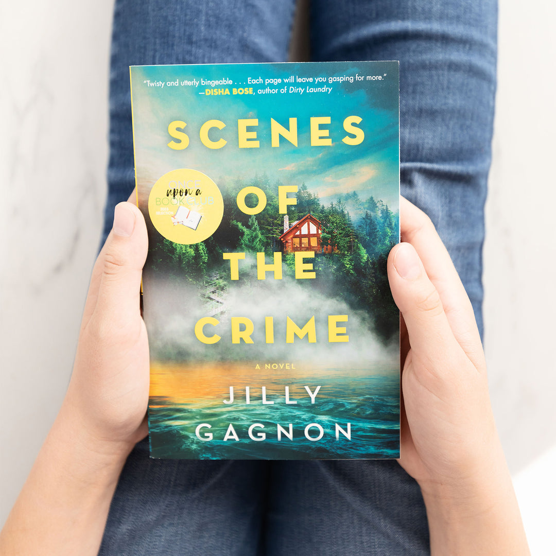 two white hands hold a paperback copy of Scenes of the Crime in their lap