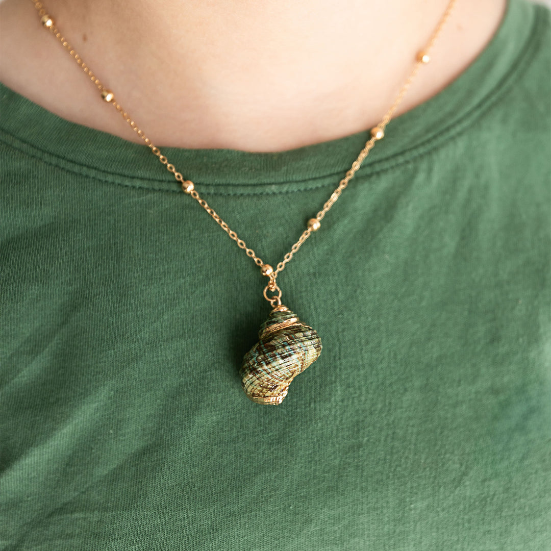 a green and gold seashell necklace with a gold chain is around the neck of a person wearing a green shirt
