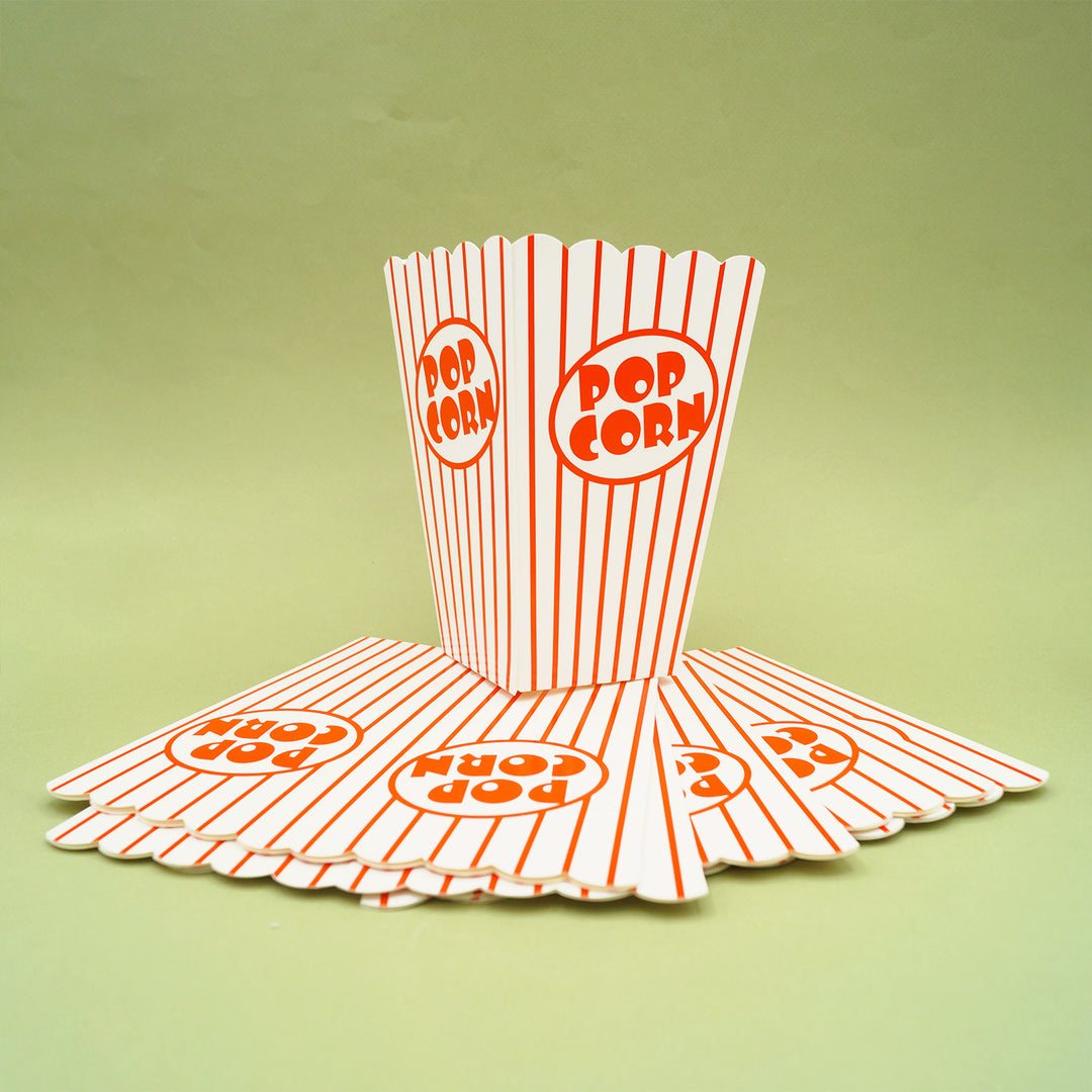 A red and white striped popcorn cup stands on a stack of other flat popcorn cups.