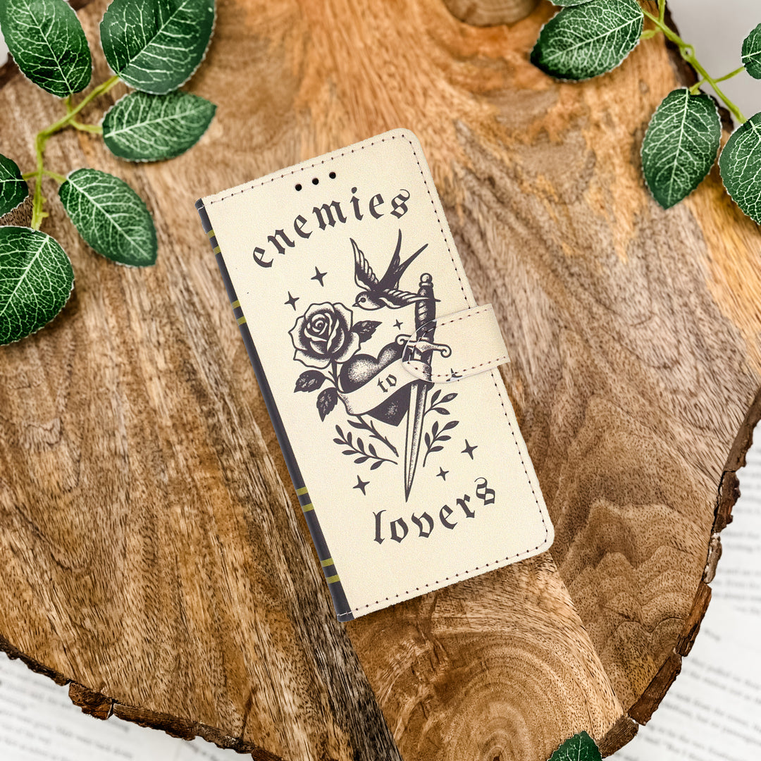 Phone case with enemies to lovers design on a wooden surface with leaves