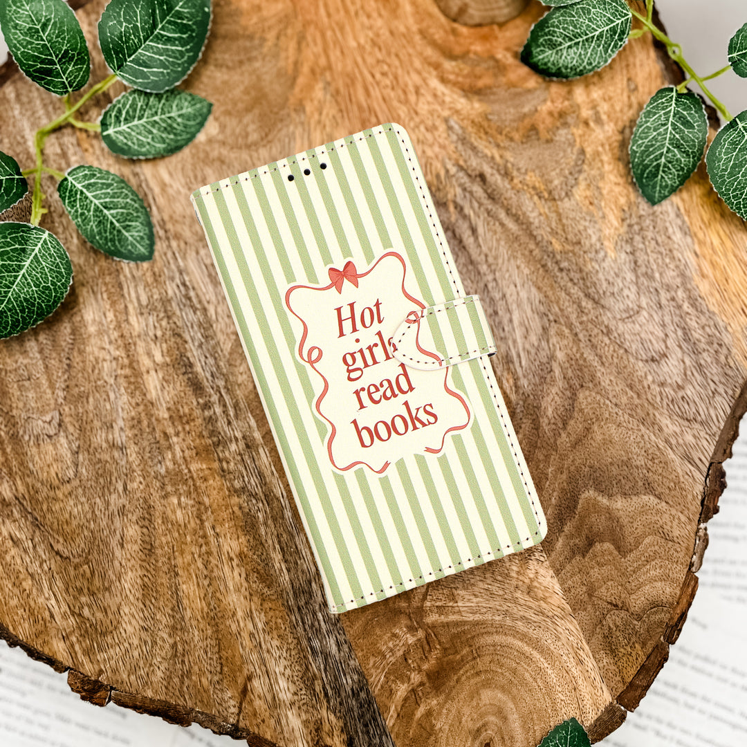 Notebook with 'Hot girl read books' text on a wooden surface with green leaves.