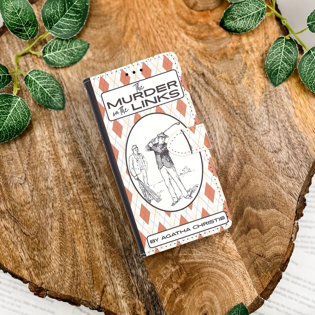 Book phone case inspired by 'Murder in the Links' by Agatha Christie on a wooden surface with green leaves.
