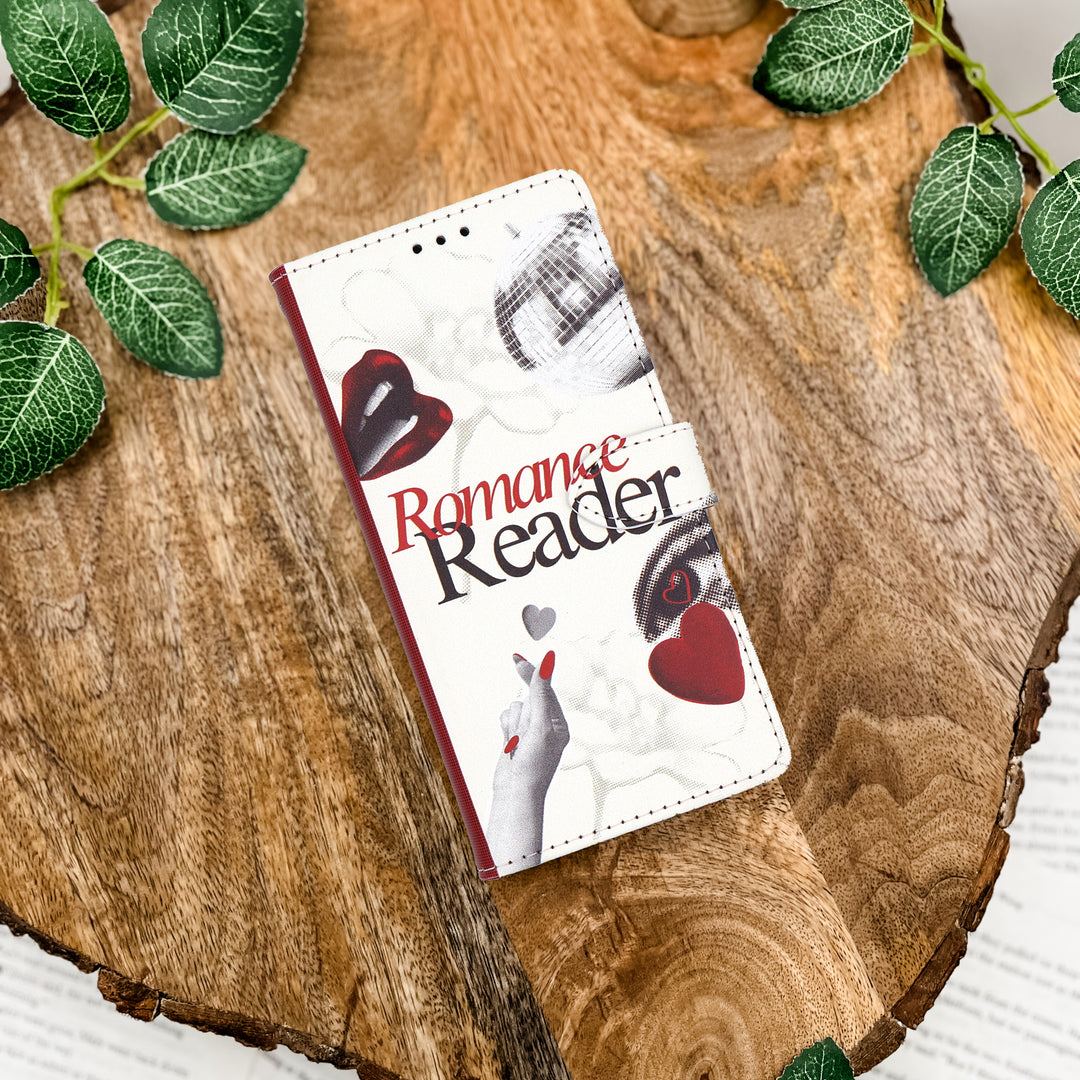 Phone case with 'Romance Reader' design on a wooden surface with green leaves.