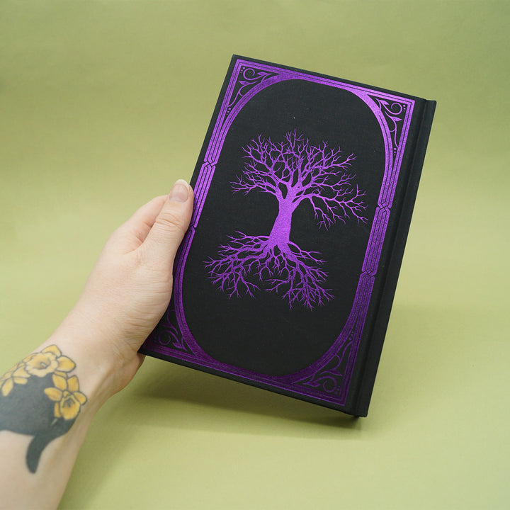 Hand holding a black book with a purple tree design on a green background