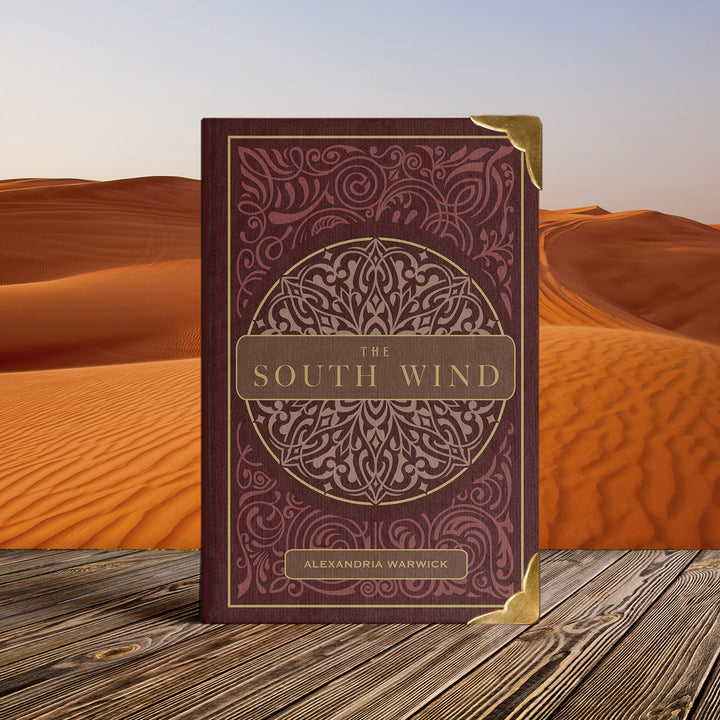 Special edition book 'The South Wind' by Alexandria Warwick featuring metal edges on a wooden surface with desert background