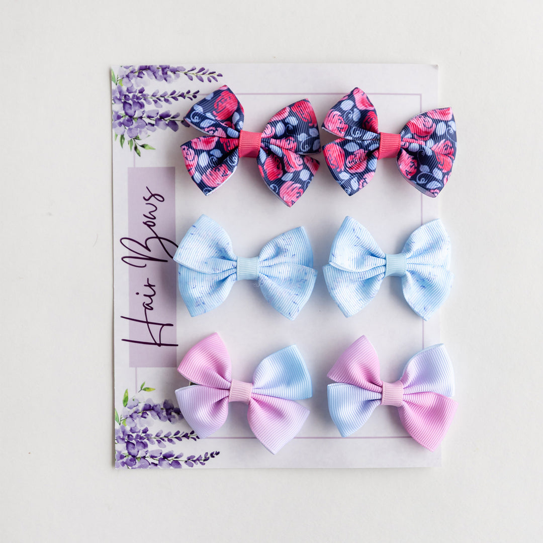 A set of six hairbows in varying colors. Two are pastel pink and blue ombre, two are light blue, and two are dark blue and red floral patterned.