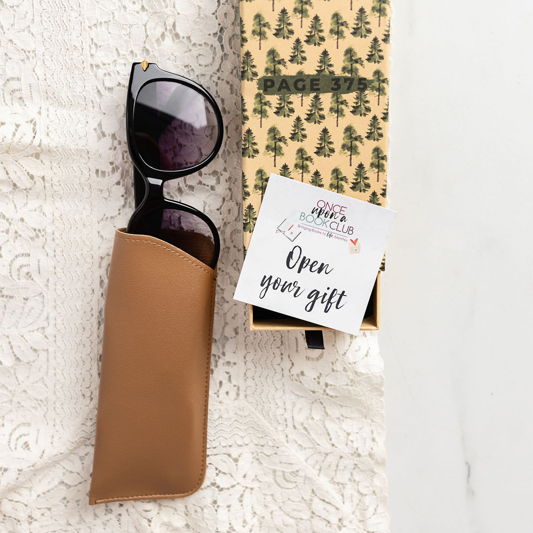 black sunglasses are coming out of a brown case next to a rectangular box with trees on it, with an "open your gift" sticker on top