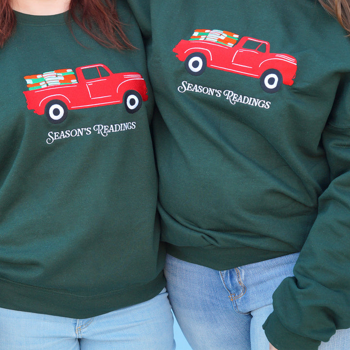 Two green sweatshirts with embroidered red truck graphics and 'Season's Readings' text on a blue background.