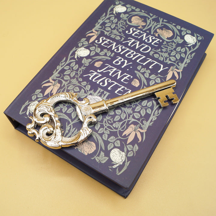 a golden key lays on a blue box in the shape of the book Sense and Sensibility by Jane Austen