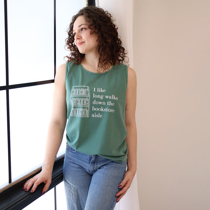 Woman wearing a green tank top with text that reads 'I like long walks down the bookstore aisle' and bookshelf graphic on a beige background.