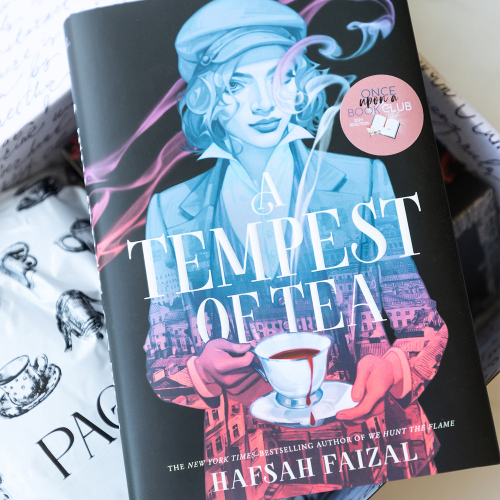 A hardcover copy of A Tempest of Tea sits on top of an open Once Upon a Book Club box containing wrapped gifts that pair with the novel.