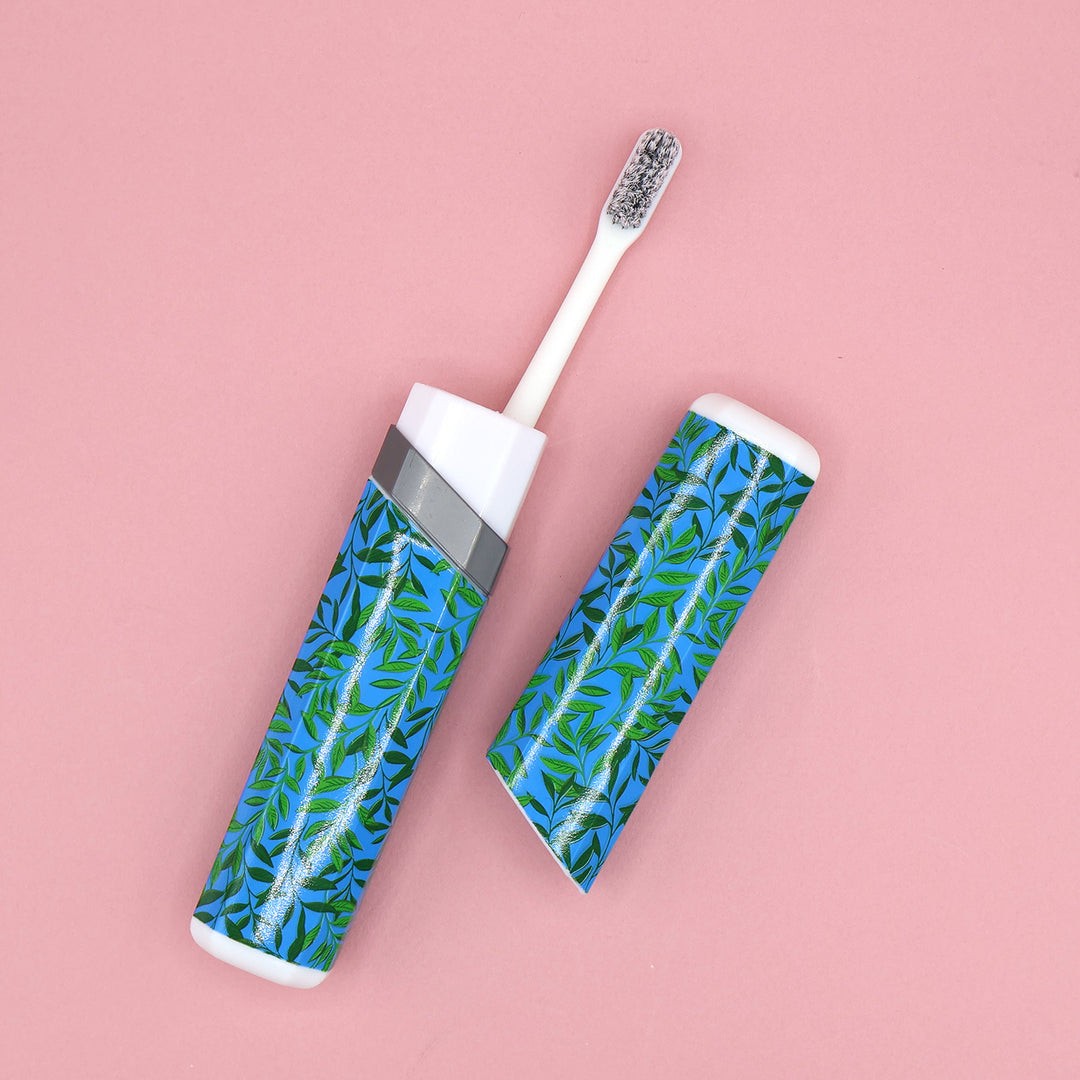 A white toothbrush sticking out of a blue travel case, next to the top half of the case. The blue case has a green leaf pattern across it.