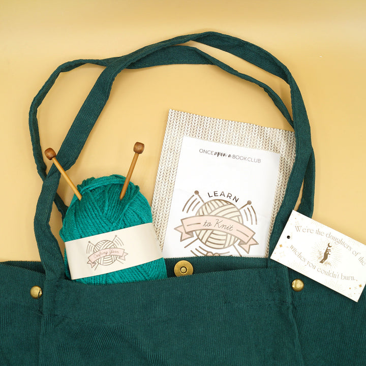 a dark green Corduroy Tote with a ball of teal yarn with knitting needles in it and a packet that says "Learn to Knit" sticking out of it