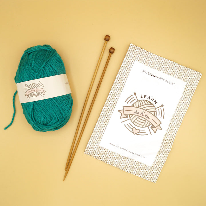 a ball of teal yarn sits next to knitting needles and a packet labeled "Learn to Knit"