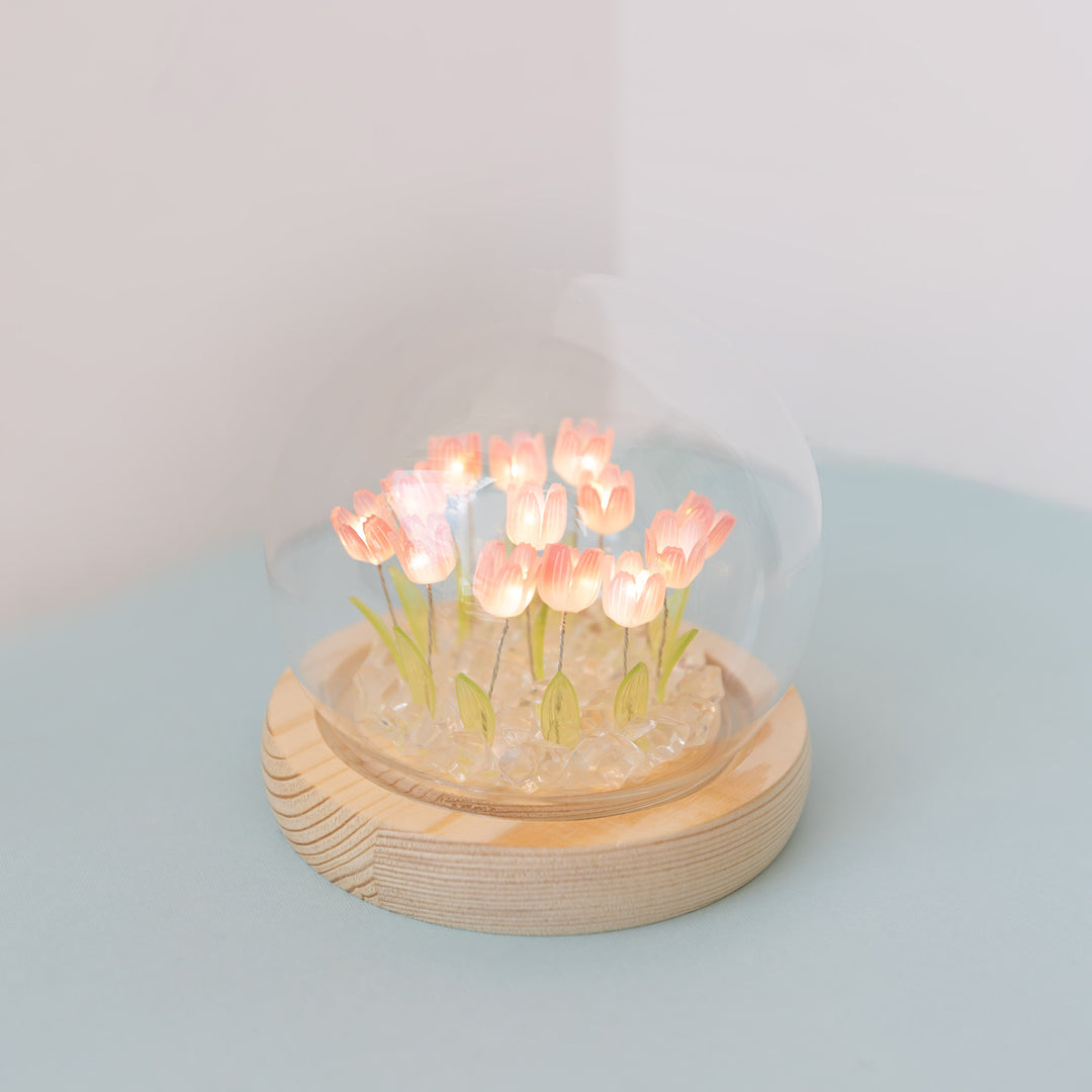 A glass dome with a wooden baseand multiple light-up pink tulips.