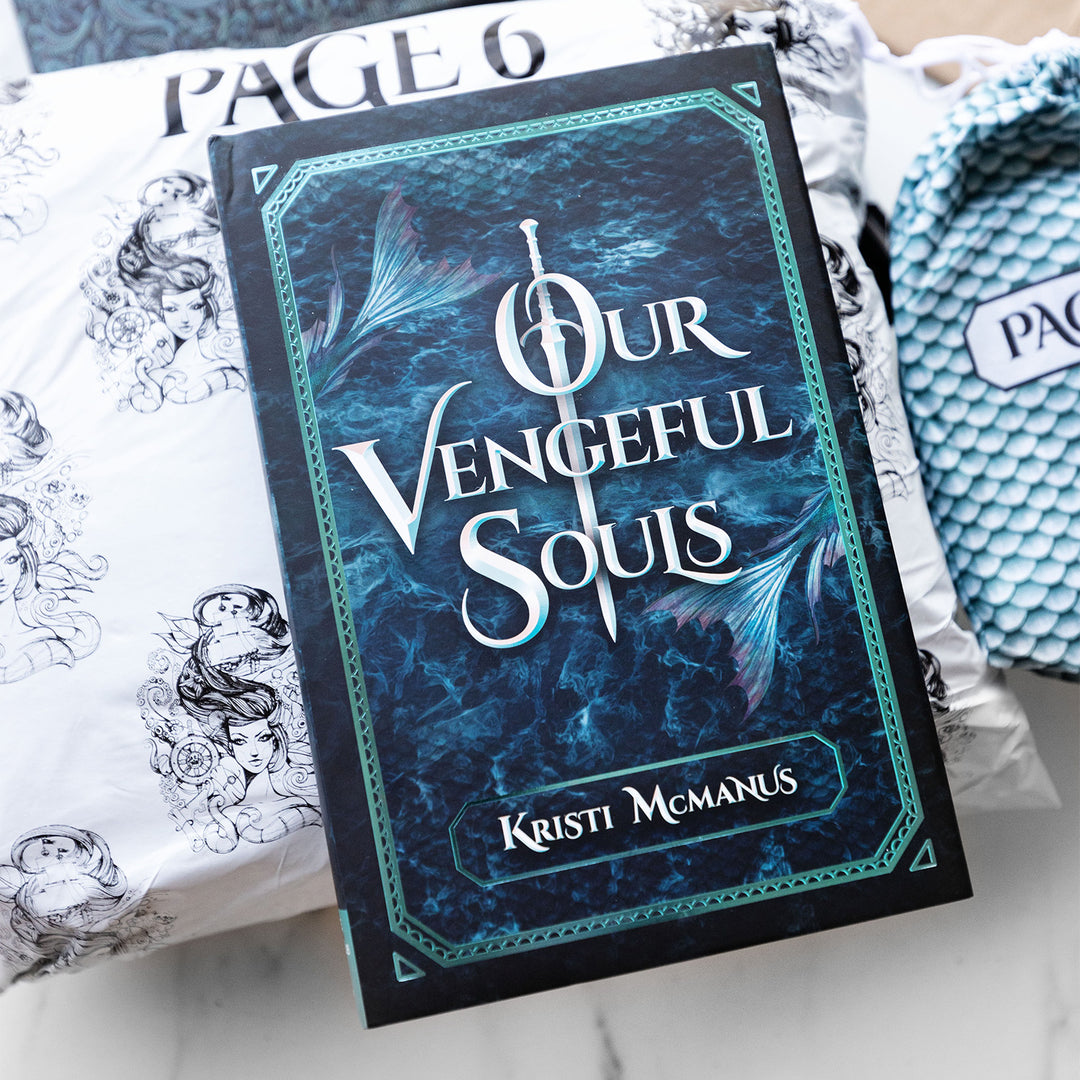 hardcover special edition of Our Vengeful Souls against a white bag. Cover shows the ocean with two mermaid tails and teal outline around the edge of the front of the book