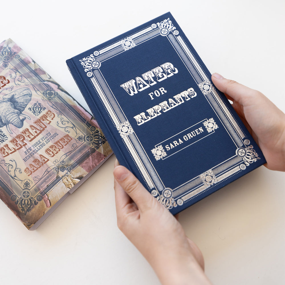 Blue fabric hard case featuring silver foil details. 'Water for Elephants' by Sara Ouen held by a hand on a light background