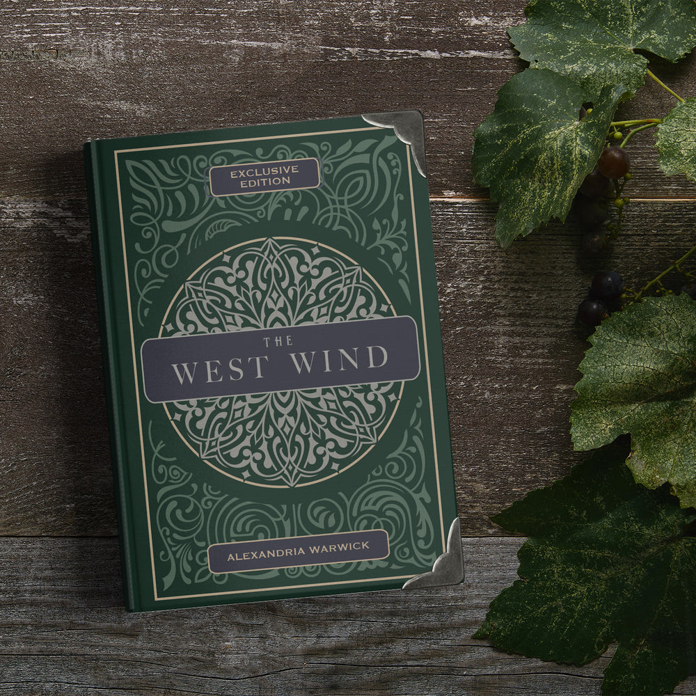 a hardcover dark green special edition of The West Wind with metal corners sits against a dark wooden board next to leaves