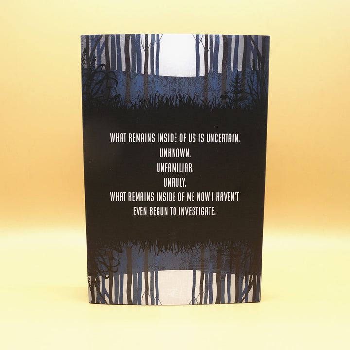 the back dust-jacket of a hardcover copy of What Remains. In white writing against a black background of trees, it says "What remains inside of us is uncertain. Unknown. Unfamilar. Unruly. What remains inside of me now I haven't even begun to investigate"