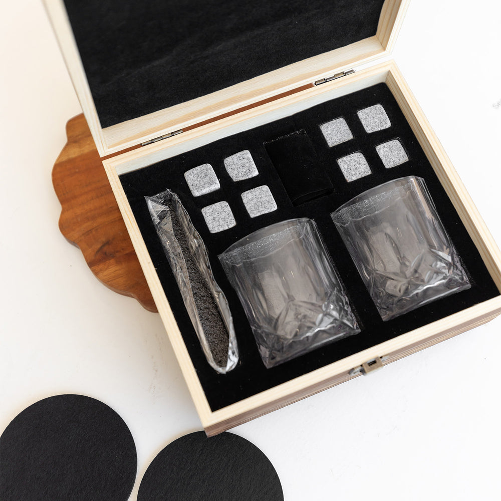 An open wooden box with two whiskey glasses, ice cubes, and tongs.