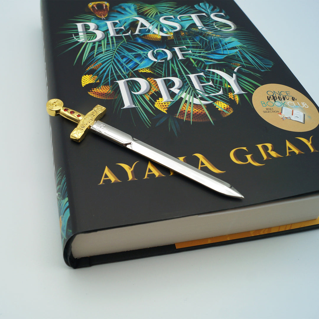 a letter opener shaped like a sword with a gold handle lays on a hardcover edition of Beasts of Prey