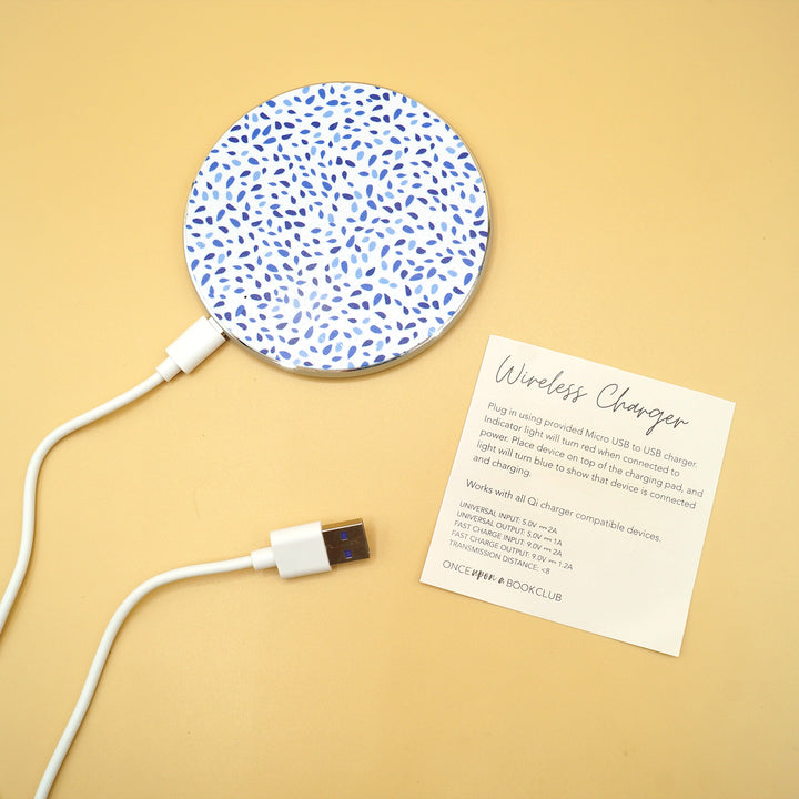 a white wireless phone charger with blue dots on it and a cord plugged in to the bottom is next to a piece of paper labeled Wireless Charger