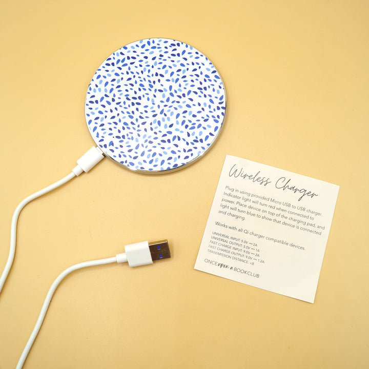 a white wireless phone charger with blue dots on it and a cord plugged in to the bottom is next to a piece of paper labeled Wireless Charger