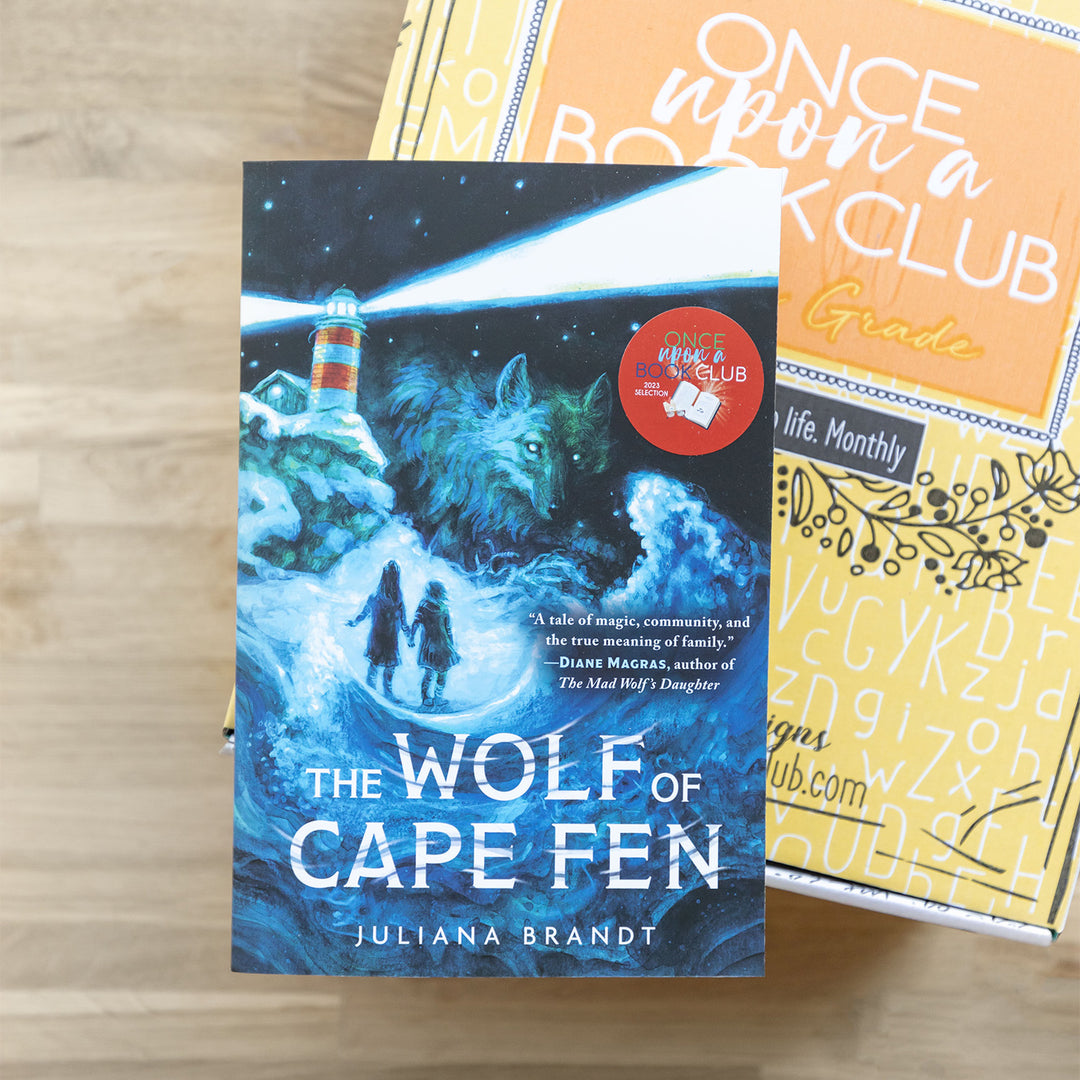 paperback edition of The Wolf of Cape Fen lays on a yellow box on a wooden table