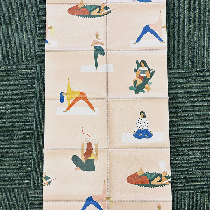 an unfolded pale pink yoga mat with cartoon images of women reading or doing yoga poses