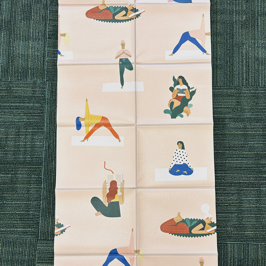 an unfolded pale pink yoga mat with cartoon images of women reading or doing yoga poses