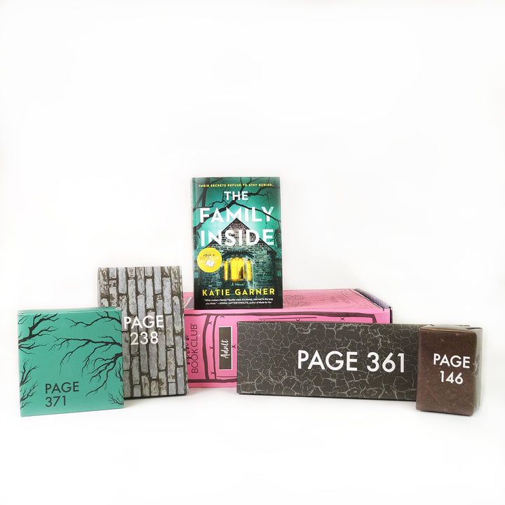 Paperback edition of The Family Inside stands on a pink OUABC box. In front of the box are four themed wrapped gifts labeled with page numbers.