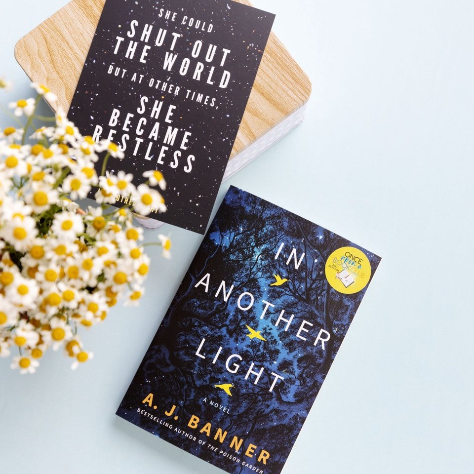 paperback edition of In Another Light next to a quote card that says "She could shut out the world but at other times she became restless" and white and yellow flowers