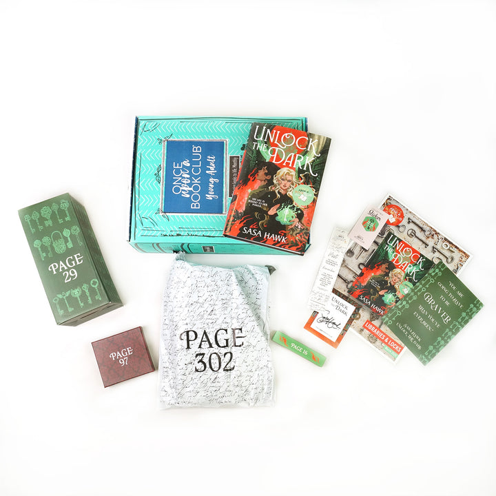 A hardcover copy of Unlock the Dark by Sasa Hawk on a green young adult OUABC box surrounded by wrapped gifts and paper items.