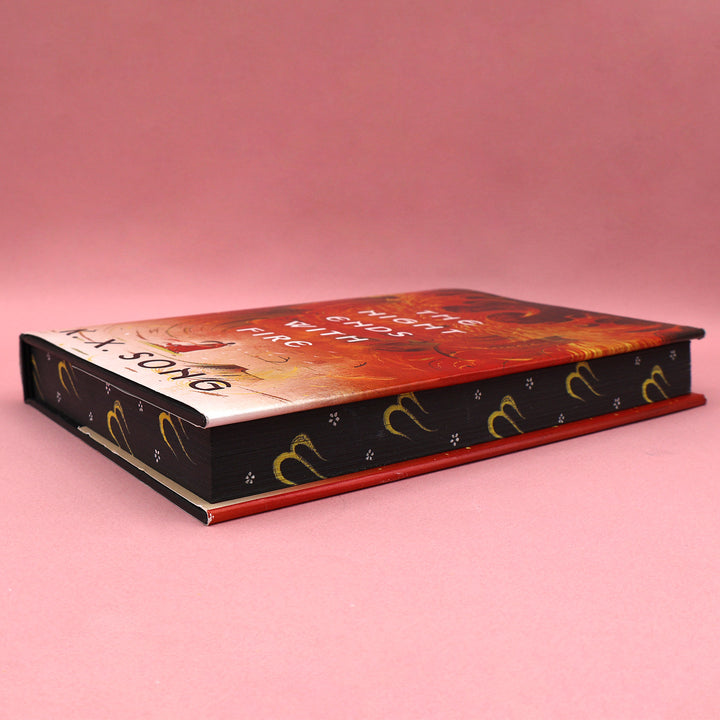 Book edges of 'The Night Ends with Fire' by K.X. Song on a pink background