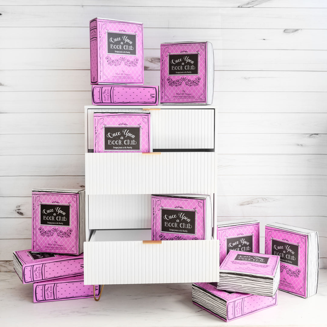 12 pink Once Upon a Book Club Adult boxes sit on and around a chest of drawers