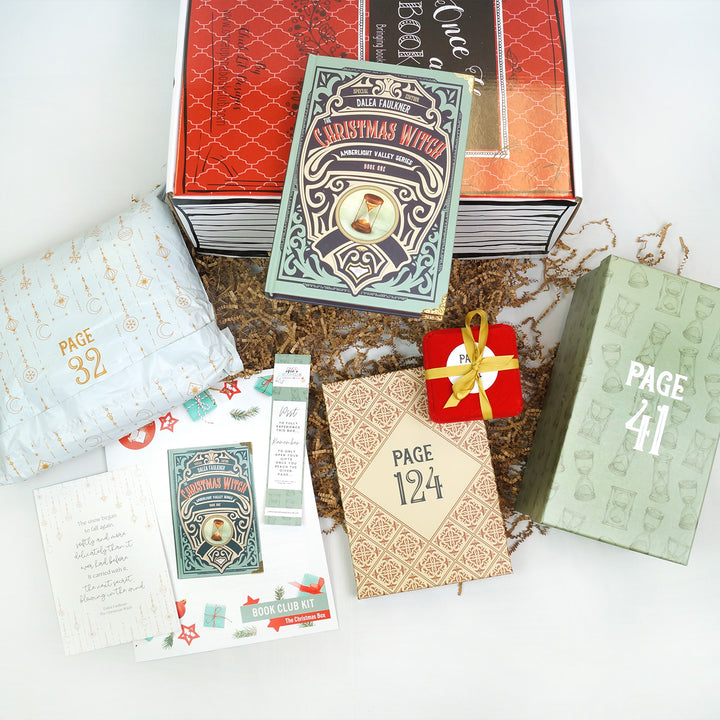 a hardcover special edition of The Christmas Witch lays on a red Once Upon a Book Club Christmas box. In front (from left to right) are a white polybag, quote card, bookclub kit, bookmark, beige box, red square box with yellow bow, and green box with hourglasses on it. The boxes and bag are all labeled with page numbers.