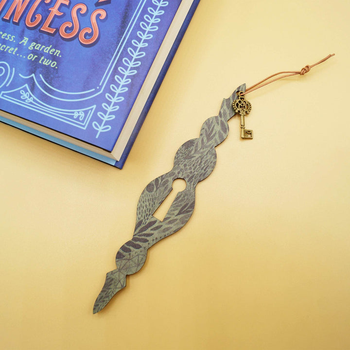 a black and dark green keyhole bookmark lays next to a hardcover edition of The Secret Princess