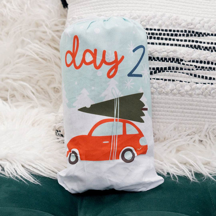 A light blue drawstring bag with a red car holding a pine tree on top, labeled Day 2