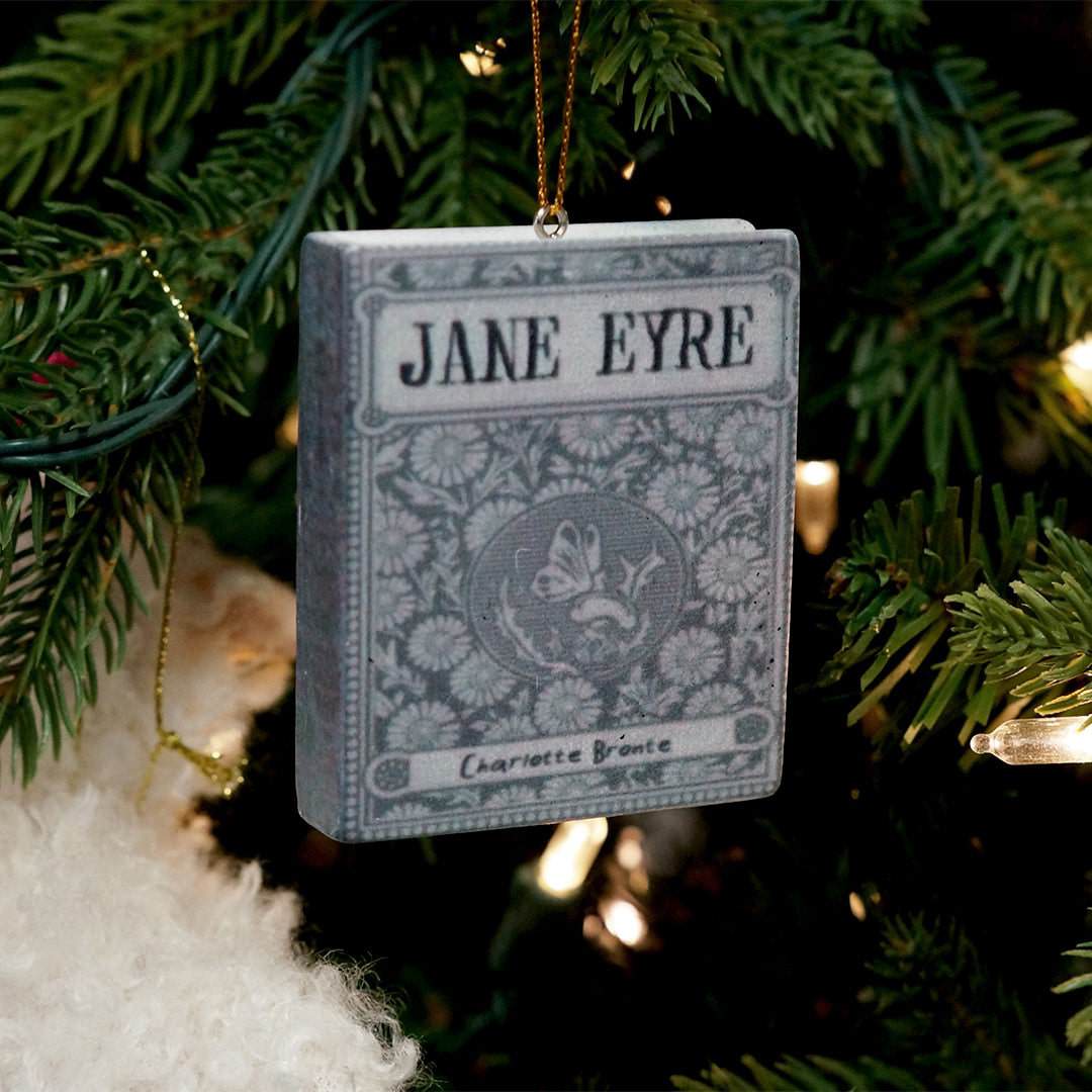 a gray ceramic book ornament with the book cover of Jane Eyre hangs off of a Christmas tree