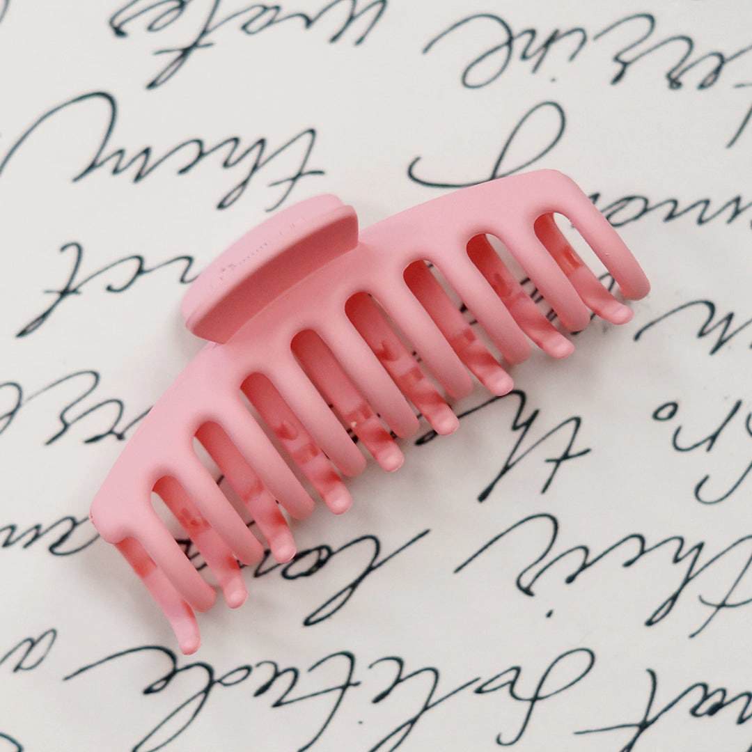 a pink hair claw clip against a white background with black script