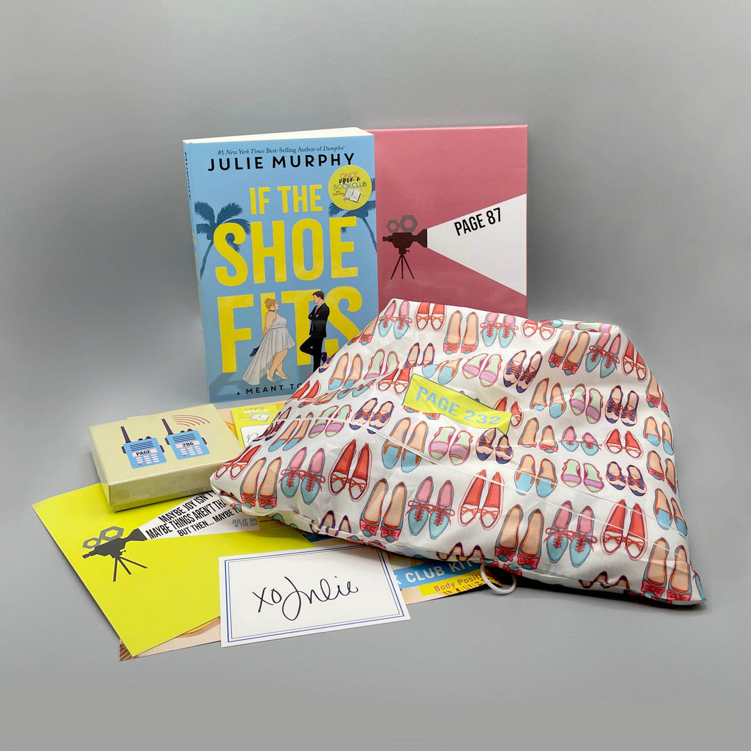 A paperback edition of If the Shoe Fits is next to a pink box. In front of the book is a yellow square box, quote card, signature card, and white drawstring bag with a pattern of shoes on it. The boxes and bags all have page numbers.