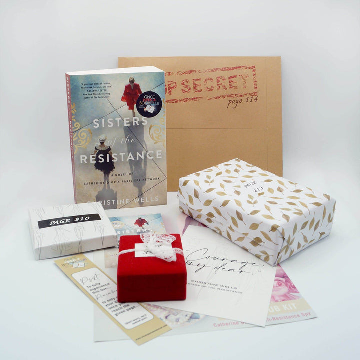 A paperback edition of Sisters of the Resistance stands next to a brown envelope labeled Top Secret. In front of the book are a white box, red box, white and gold box, and pile of paper items. The boxes all have page numbers.