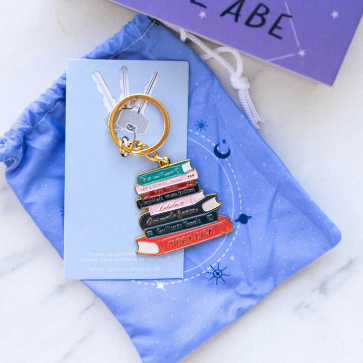 a book stack keychain with gold ring lays on a blue drawstring bag