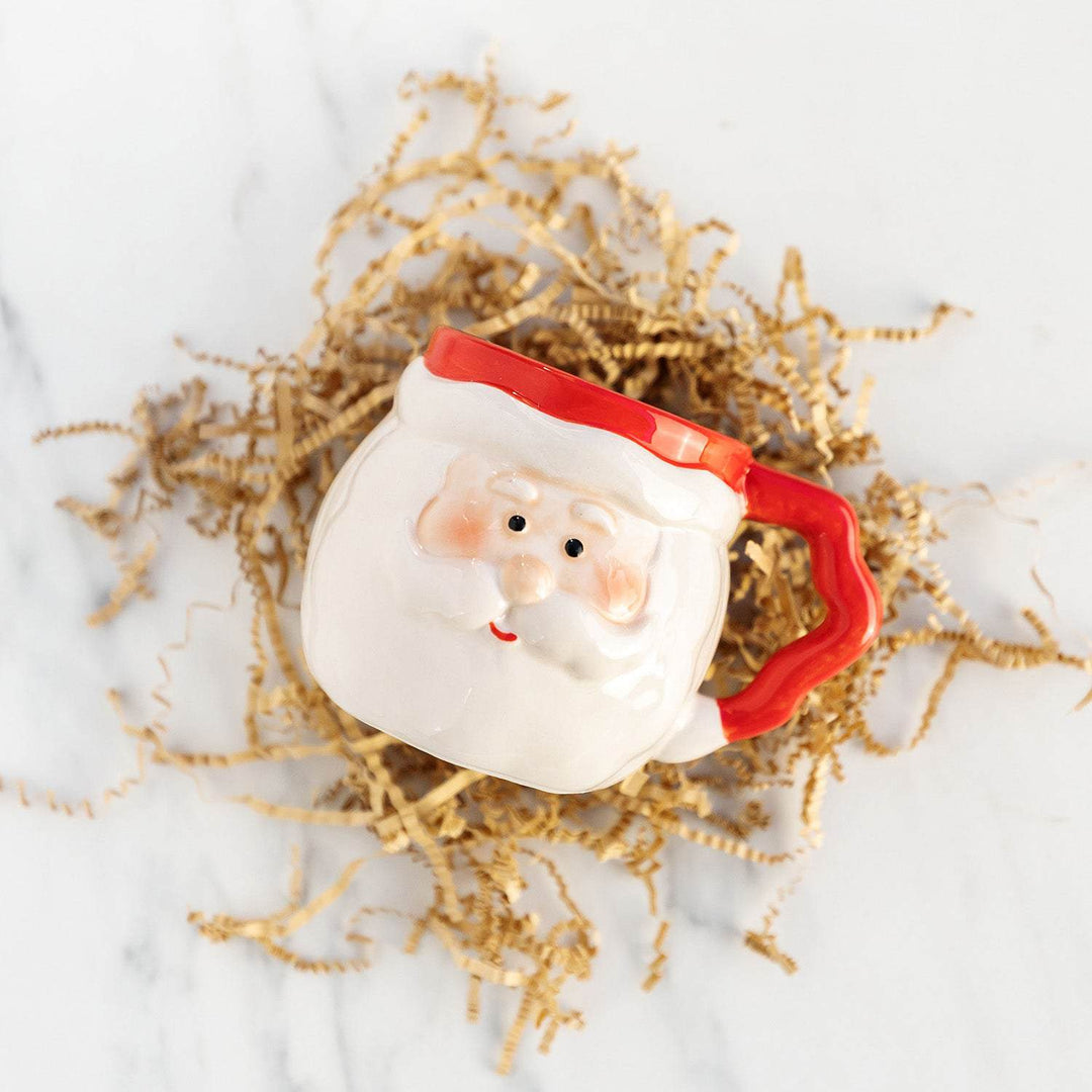a mug shaped like Santa lays on a pile of brown crinkle paper