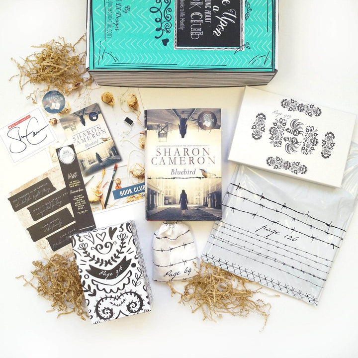 A hardcover edition of Bluebird is centered in the photo surrounded by two white and black boxes, white polybag, white drawstring bag, green Once Upon a Book Club box, and an assortment of paper items