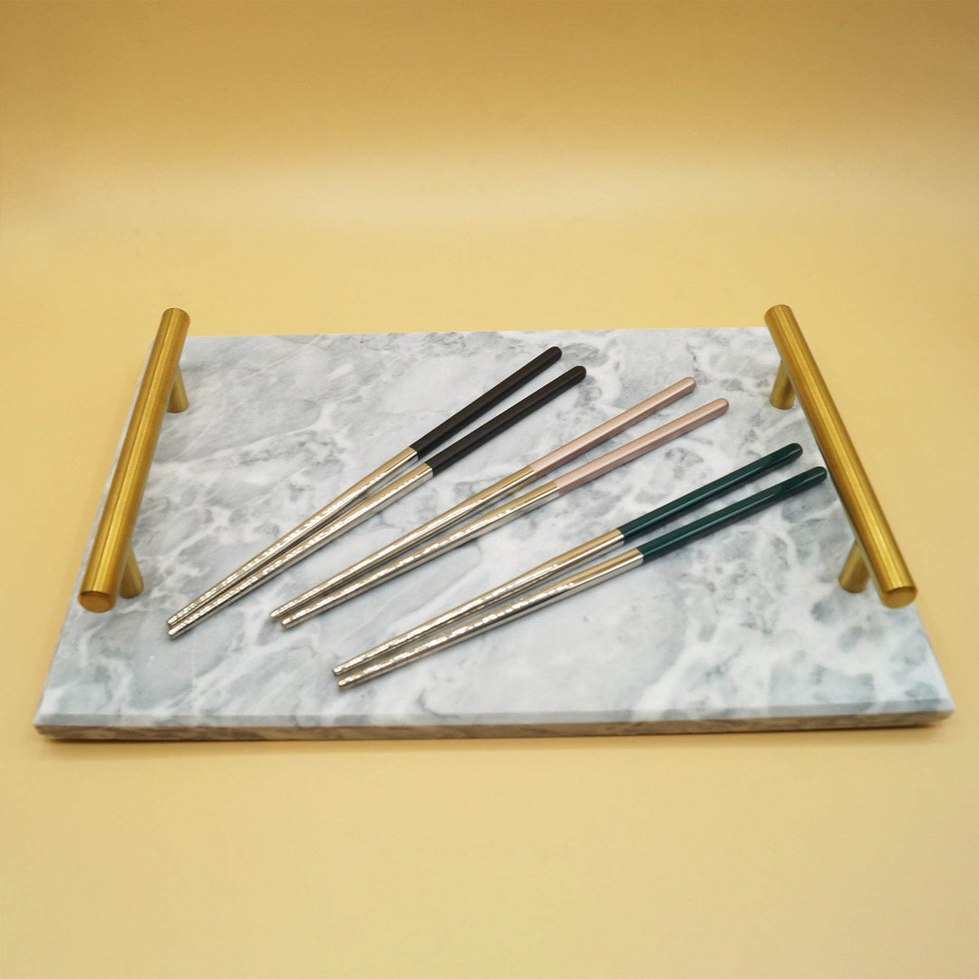 three sets of chopsticks lay on a gray marble tray with gold handles