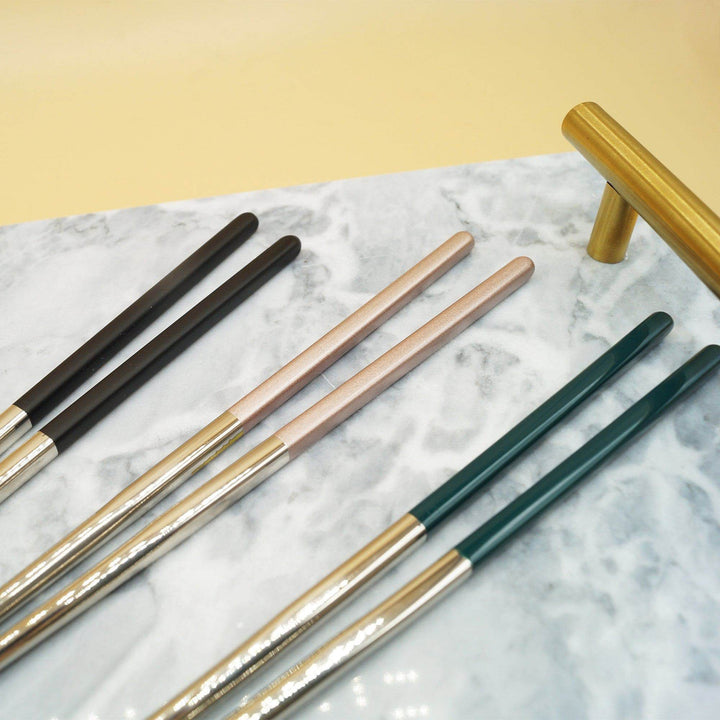 Three sets of chopsticks lay on a marble tray with gold handles