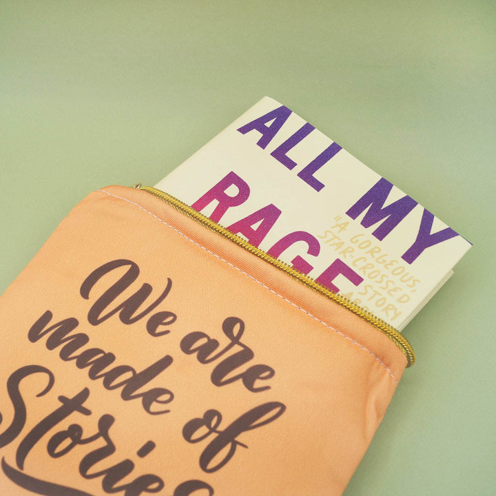 a peach-toned book sleeve with gold zipper closure. On the front is the quote "We are made of stories" and a hardcover edition of All My Rage is coming out of the top