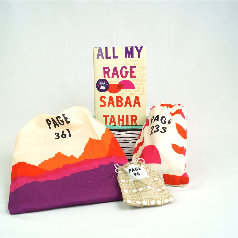 A hardcover edition of All My Rage is on top of a green Once Upon a Book Club box. In front of the box are two white drawstring bags and one gold and white drawstring bag. The bags all have page numbers.