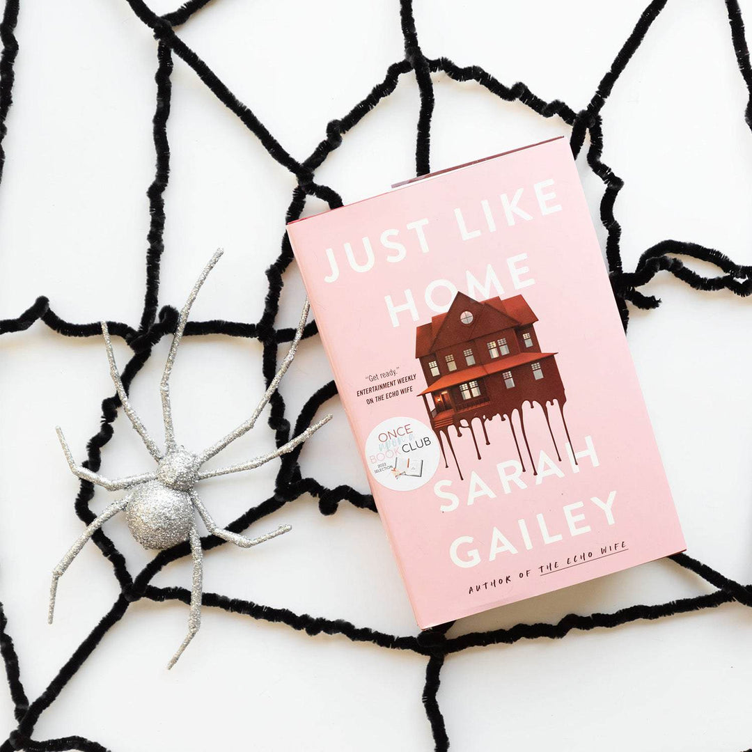 a hardcover edition of Just Like Home lays on a black felt spider web next to a fake silver sparkly spider